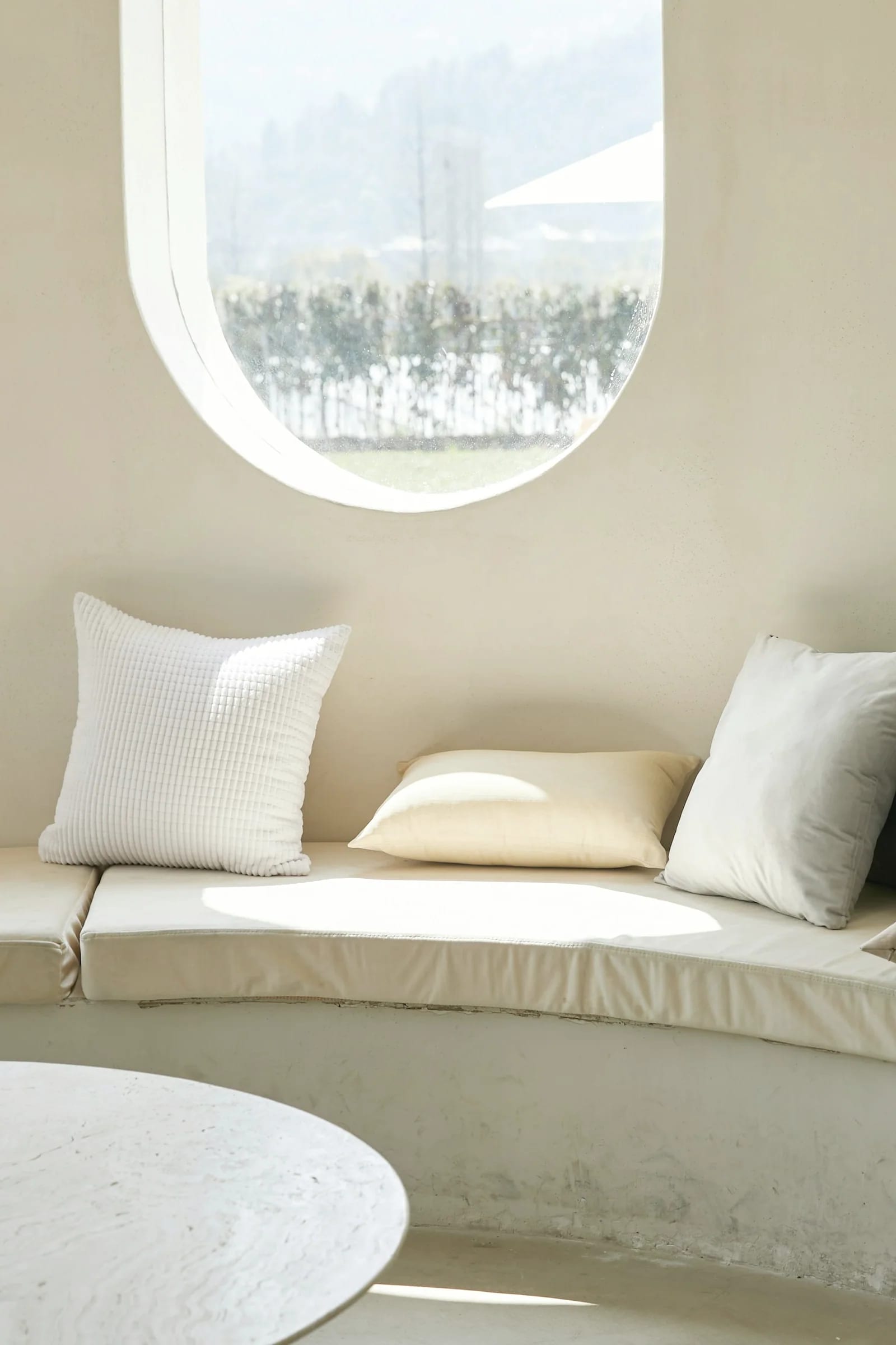 A built-in daybed under a round window in a warm plastered room