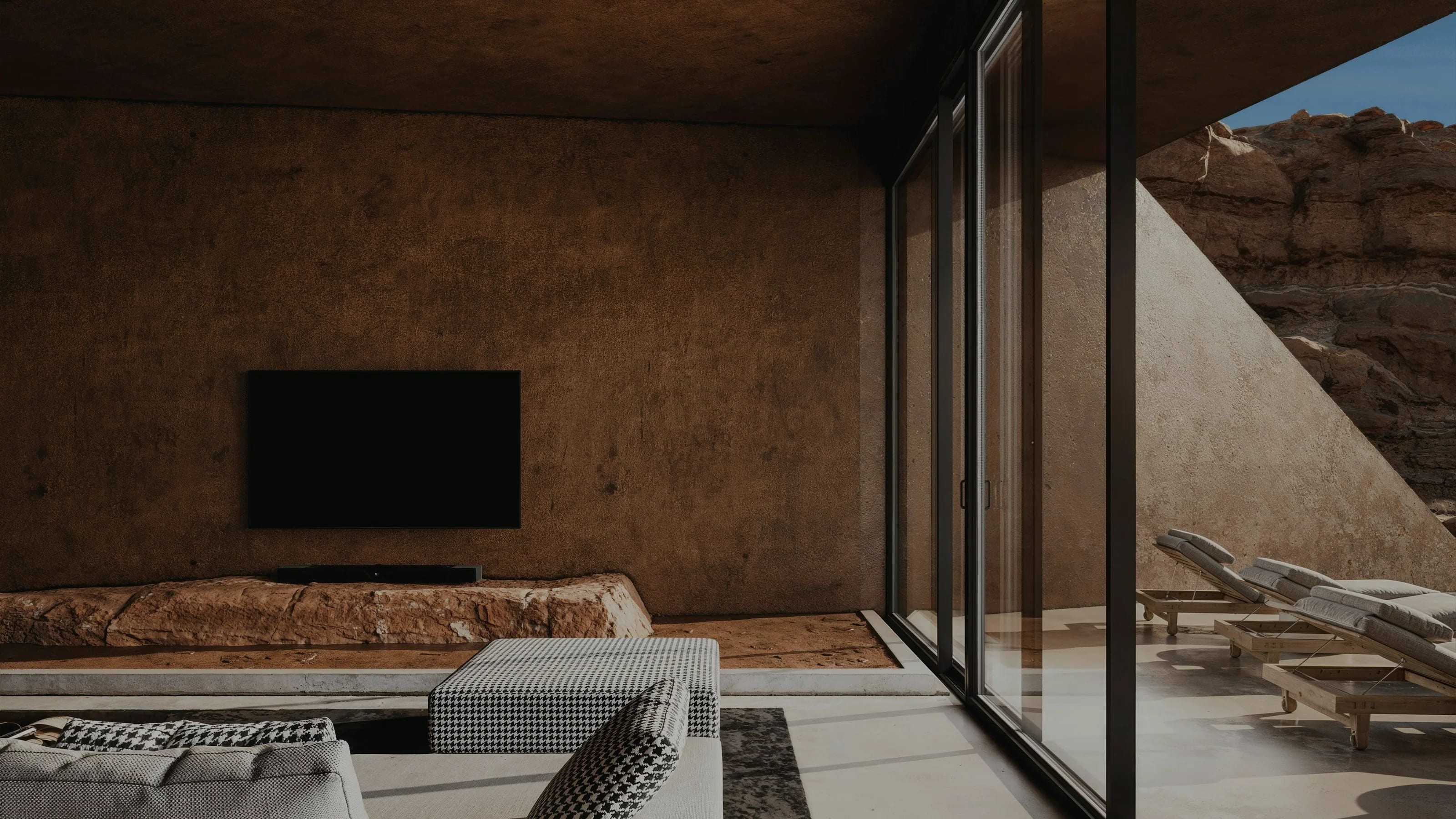 A concrete living room opening onto a canyon through full-height glazing